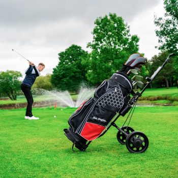 male golfer taking a swing behind a red golf trolley