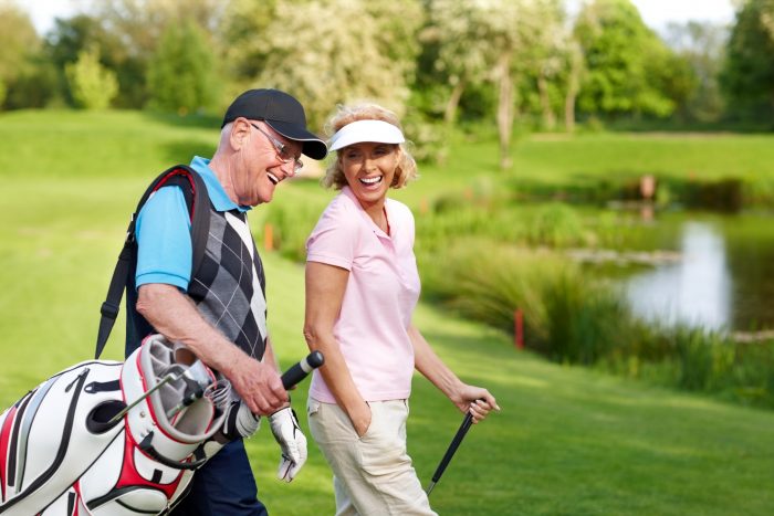 male and female senior golfers laughing carrying golf clubs