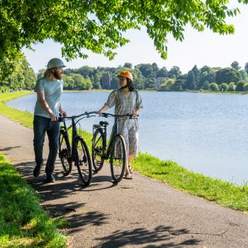 Two people pushing a Dawes electric bike along a river.