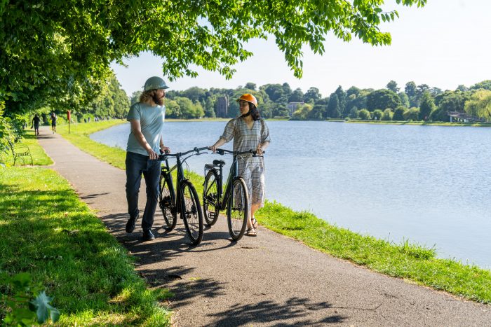 Two people pushing a Dawes electric bike along a river.