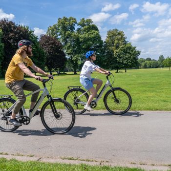 Two people riding a Dawes electric bike along a field of grass