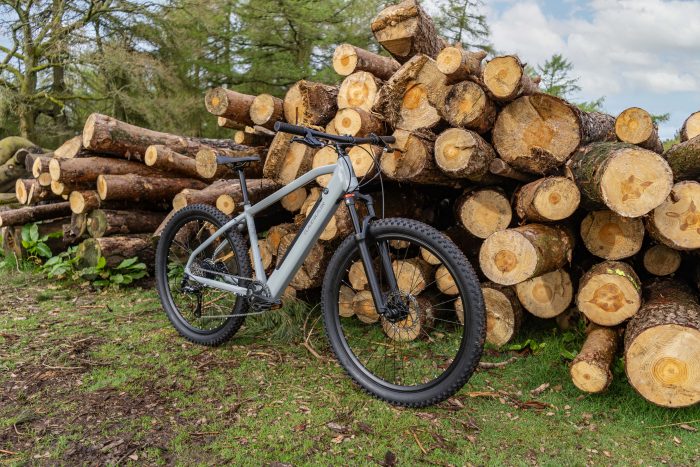 Light grey electric bike stood up against a pile of logs in a field