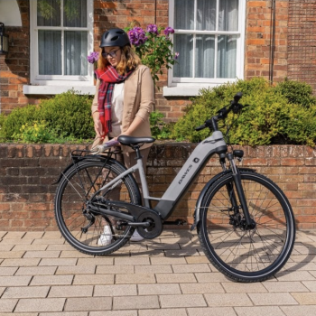 image of a dawes hybrid bike resting against a brick wall with a women in a beige coat andred tartan scarf