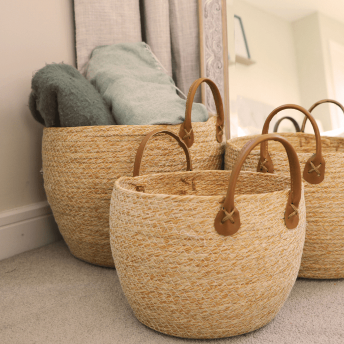 Three woven baskets are placed on the floor beside a tall mirror, reflecting their shapes and textures.